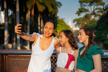Tourists taking a selfie in one of the bridges along the Cali River Boulevard with La Ermita church on background in the city of Cali in Colombia. Mother and teenager daughters traveling concept.
