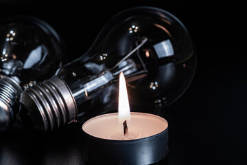 Electric lamp and candle on a dark background. Incandescent lamp and candle. No or power outage. High electricity prices. Saving electricity.