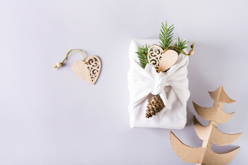 Furoshik with fir branches and wooden hearts and cardboard fir trees on a gray. Eco-Friendly Gifts