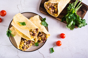Burrito with minced meat, corn, beans and tomatoes in corn tortillas on a plate. Top view