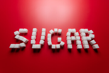 the word sugar is made up of sugar cubes on a red background. photo on the topic of the dangers of eating refined sugar