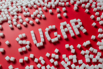 the word sugar is made up of sugar cubes on a red background. photo on the topic of the dangers of eating refined sugar