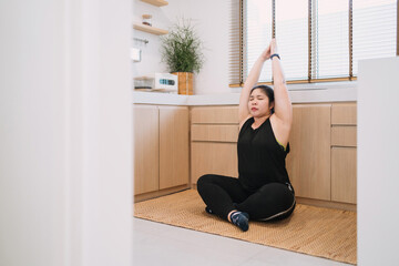 fat woman meditating yoga raising hand in kitchen. overweight warm female person meditating controlling mind raising arm. overweight spiritual woman doing yoga activity hand pose care body and mind