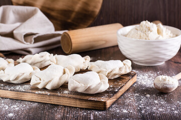 Raw dumplings on a cutting board and flour on the table. Home cooked food.
