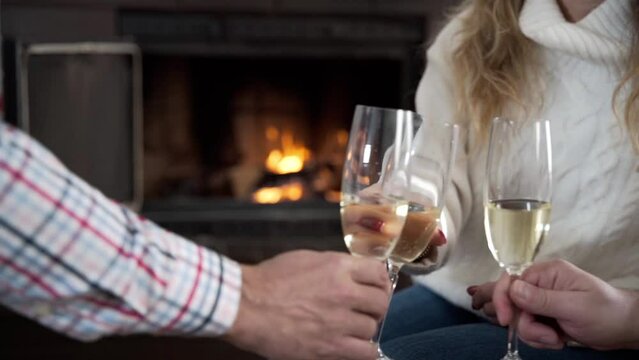 Close-up of hands clinking glasses. A small group of people clink glasses of champagne by the fireplace