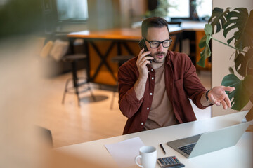 A male business person with beard, dressed in casual cloths is having a phone call with his...