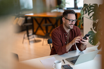 Shot of a young businessman using a smart phone in a home office. Smiling, touching the screen, browsing the internet.