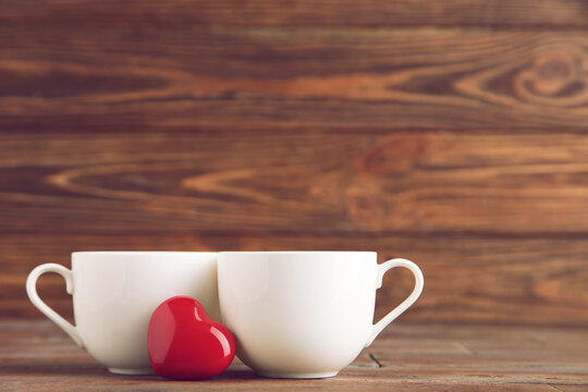 White cups and red heart on brown wooden background