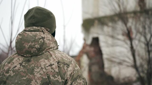 Soldier of the Armed Forces of Ukraine in a winter uniform with a trident walks on the territory of a destroyed factory in a war zone. Consequences of the war in Ukraine.