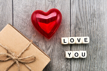 gift in a box and an inscription from wooden cubes LOVE YOU. Red heart on a gray background.