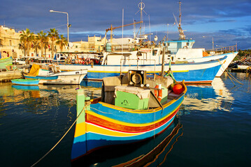 Traditional fishing boats luzzu in Marsaxlokk village in Malta, painted in bright colours – blue, red and yellow. Warm, afternoon sunlight