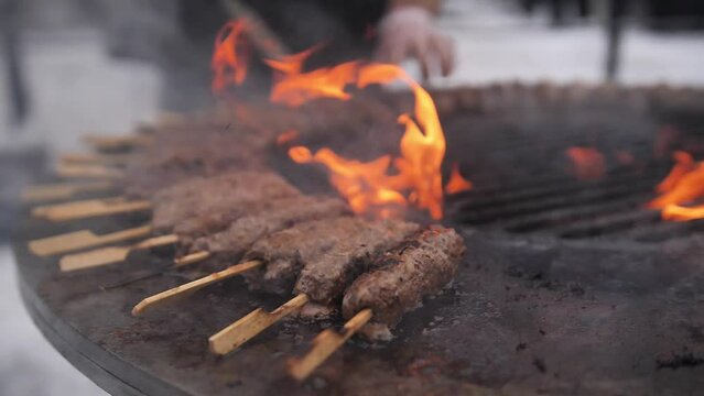 Turkish kebab is cooked on a circular grill in the open air. Close-up of the grill fire while cooking meat on skewers on the grill.