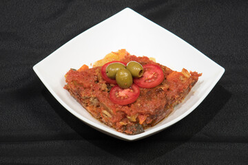 Potatoes and meat with vegetables in tomato sauce on a white plate