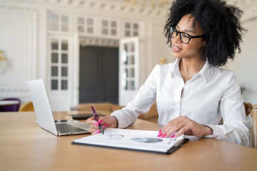 A woman with glasses and a white shirt in the office is typing a message using a laptop education. A freelancer is working on a new online project site.