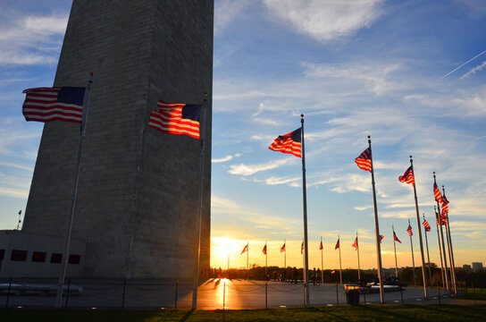 Washington Monument and waving US flags and people in silhouettes during  sunset - Washington DC - United States