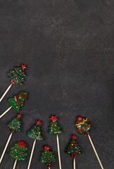 Christmas trees. Cute festive candies covered with colored icing sugar on a wooden stick. New Year. Dark gray background. Top view. Copy space