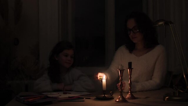 Mom in the dark lights candles in a dark room due to a power outage so that her daughter can see her coloring books.