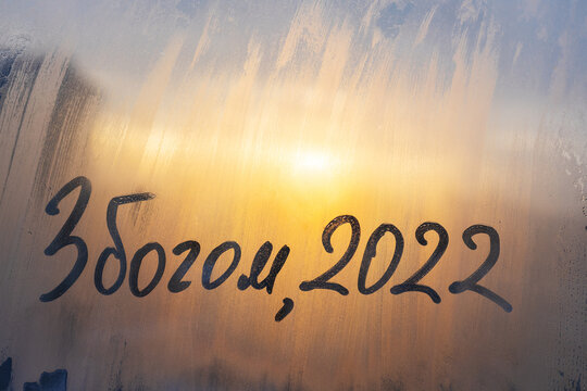 lettering goodbye in Serbian and numbers 2022 paint with finger of water on splashed by frost foggy glass on sunset window