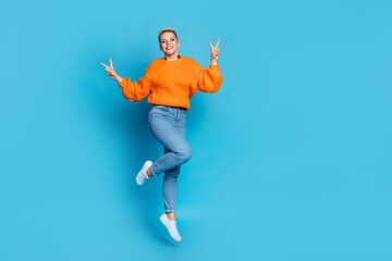 Fototapeta premium Full length photo of pretty sweet lady wear orange sweatshirt jumping high v-signs empty space isolated blue color background