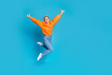 Fototapeta na wymiar Full length photo of sweet cheerful lady wear orange sweatshirt jumping high rising arms empty space isolated blue color background