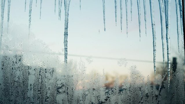Frozen window with long icicles against a sunset. View from indoors