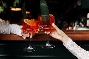 hands of woman and man are clinking, cheers with glasses of Spritz cocktail. Couple celebrating...