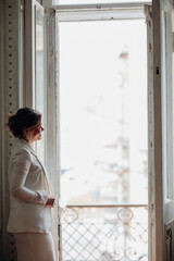 a beautiful, confident woman in a white suit at the old window. image of bride