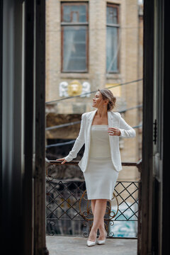 a beautiful, confident woman in a white suit on the balcony of the old building.