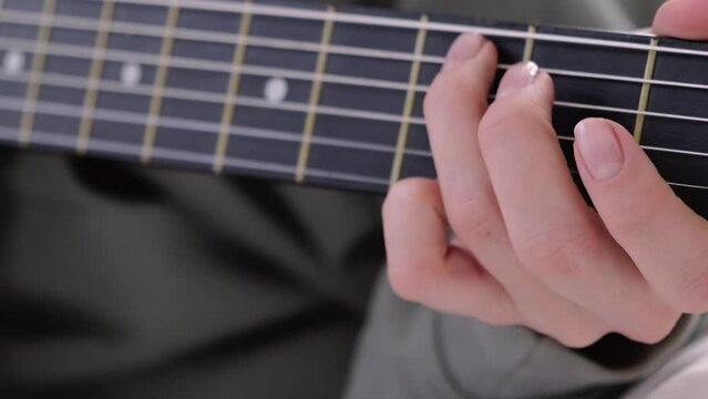 hands close up, girl pinches chords with her fingers, playing acoustic classic guitar, singing song and relaxing at home