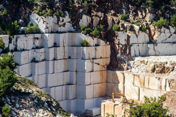 An open-pit mine of white marble stone with heavy machinery used to extract and mine the precious stone for further use and production