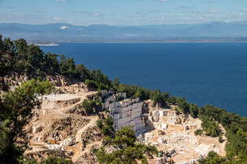 An open-pit mine of white marble stone with heavy machinery used to extract and mine the precious stone for further use and production