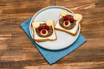 Funny bear face sandwich toast bread with peanut butter, cheese and raspberry on plate napkin wooden background. Kids child sweet dessert breakfast lunch food close up