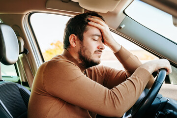 Side view young male driver closed his eyes and rests with his hand on the steering wheel and the...