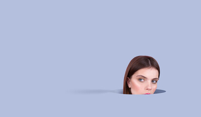 Close-up Android face of young woman with BLUE EYES natural make-up, head sticking out of a hole in the background isolated, blue background Spays for infographics or text 