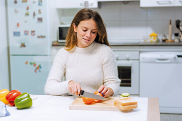 Vegetarian woman cooking a vegetable sandwich at home. cutting tomato slices