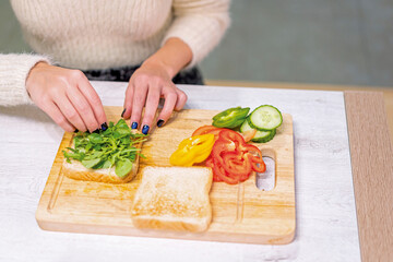 Unrecognizable person cooking a vegetable sandwich in the kitchen at home. Placing the arugula