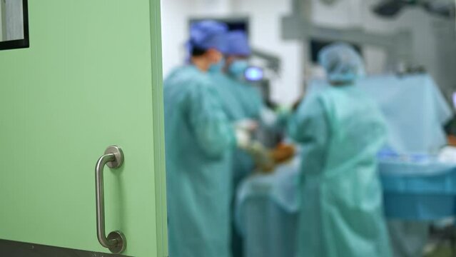 Opened door with a metal handle in hospital. Surgeons team conducting surgery inside the operational room.