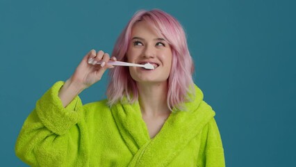 Close up head shot young happy female with pink hair brushing teeth with toothbrush and toothpaste. Smiling beautiful girl enjoying morning oral anti cavity hygienic routine alone in bathroom 4K