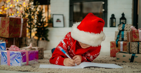 Little boy in santa hat writes a letter to santa claus