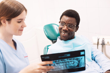 Female dentist showing teeth x-ray to male at dental clinic office.