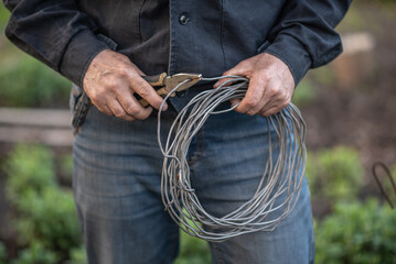 the worker is holding pliers and a roll of metal wire