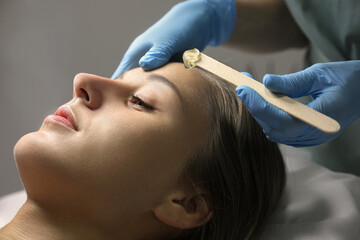 Naklejka premium Young woman undergoing hair removal procedure on face with sugaring paste in salon