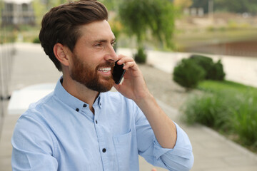 Handsome man talking on phone outdoors, space for text