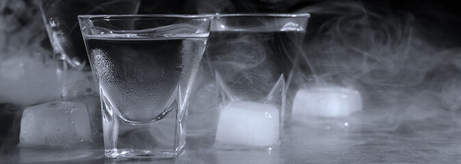 Vodka in shot glasses with ice on table against black background, closeup. Banner design - obrazy, fototapety, plakaty