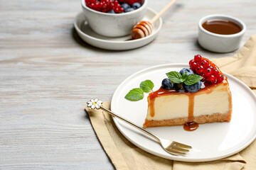 Slice of delicious cheesecake served with berries and caramel sauce on white wooden table, space...