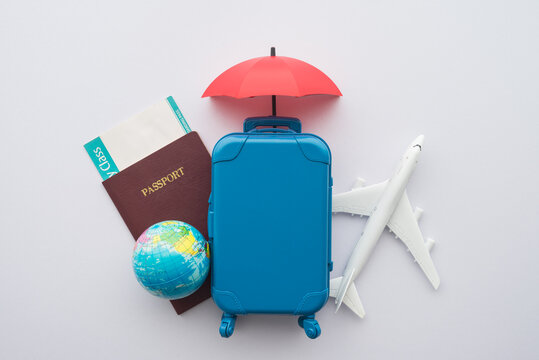 Red umbrella cover airplane, passport, globe, flight tickets and suitcases travelers on white background. Travel insurance covers loss suitcase, flight delays, cancellation, accident, medical expenses
