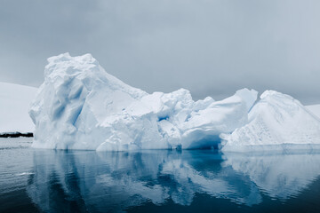 Iceberg floating off Enterprise Island in the Antarctic, with mirror. Reflection in the southern Ocean, with winter colors of grey, white, and blue.  - obrazy, fototapety, plakaty