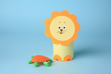 Toy lion made from toilet paper hub and plasticine turtle on light blue background. Children's...