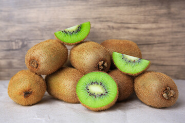 Heap of whole and cut fresh kiwis on parchment paper near wooden wall