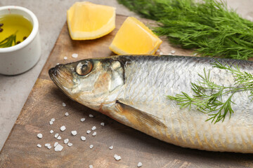 Board with delicious salted herring, dill, lemon and olive oil on grey table, closeup